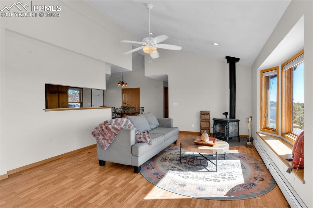 Image 9 of 50: Living room with baseboard heating, a wood stove, light wood finished floor