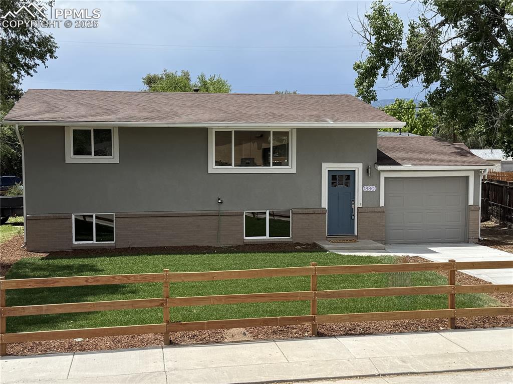 Caption: Split foyer home with a fenced front yard, a garage, stucco siding, brick siding, and a shingled roo