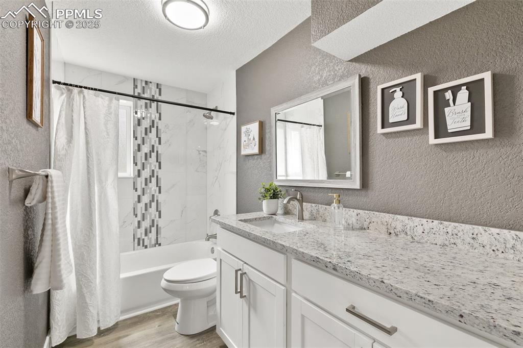 Image 10 of 18: Full bathroom featuring a textured wall, vanity, wood finished floors, a te