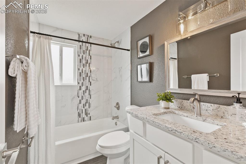 Image 14 of 18: Bathroom featuring a textured wall, vanity, and shower / bath combo with sh