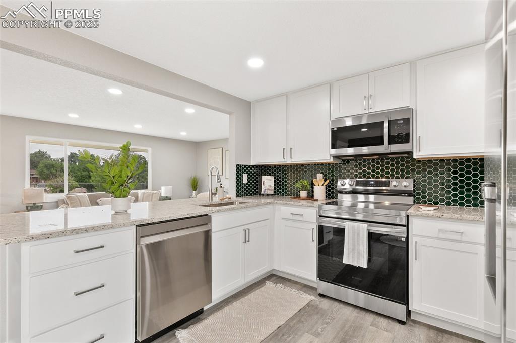 Image 8 of 18: Kitchen featuring stainless steel appliances, backsplash, white cabinetry,