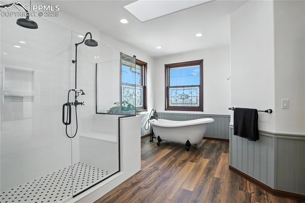 Image 22 of 50: Bathroom with a shower stall, wainscoting, a freestanding tub, a skylight,