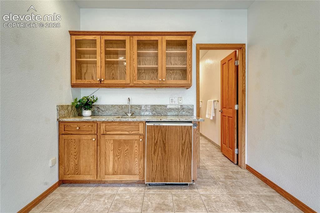 Image 36 of 50: Wet bar with granite counters and beverage fridge.