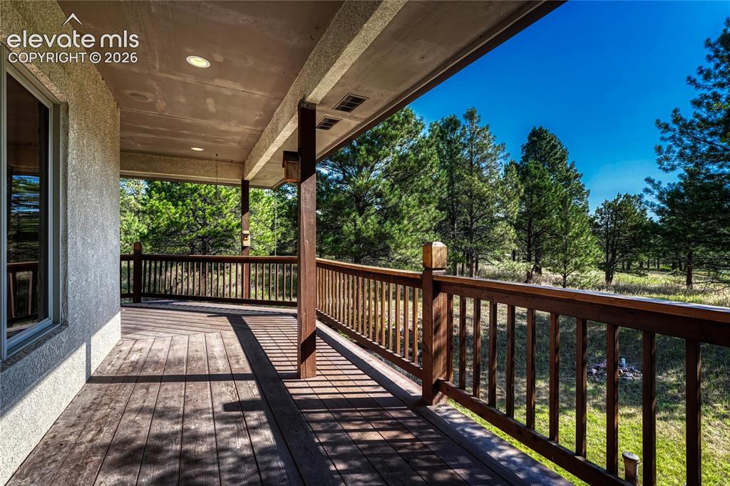 Image 8 of 50: Covered wraparound wood deck along the back and side of the home.