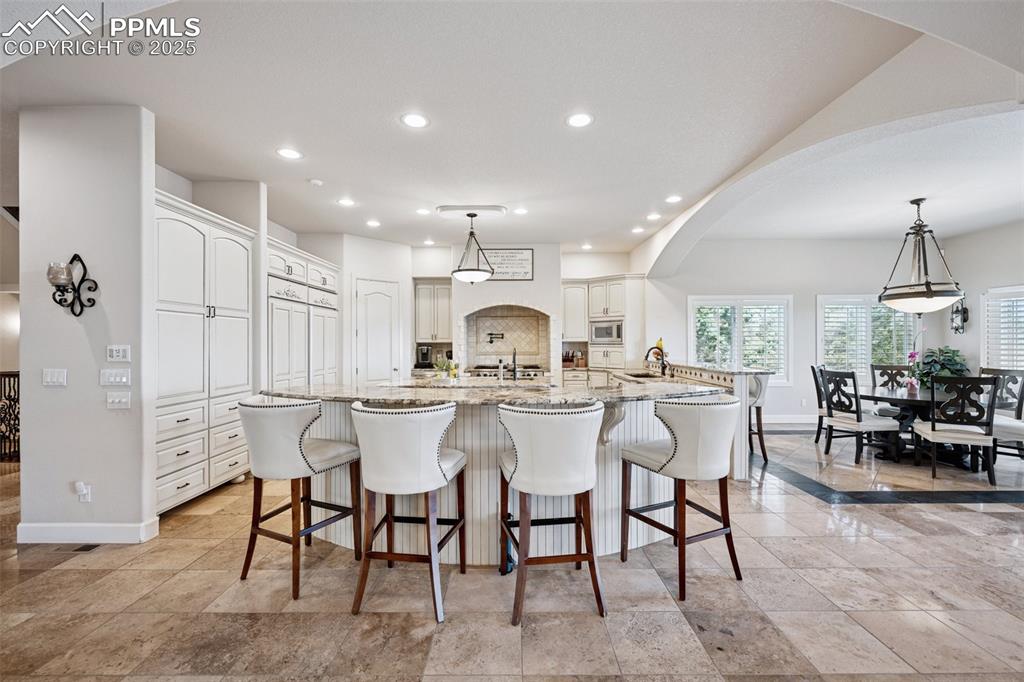 Image 14 of 48: Kitchen featuring arched walkways, baseboards, light stone counters, and re