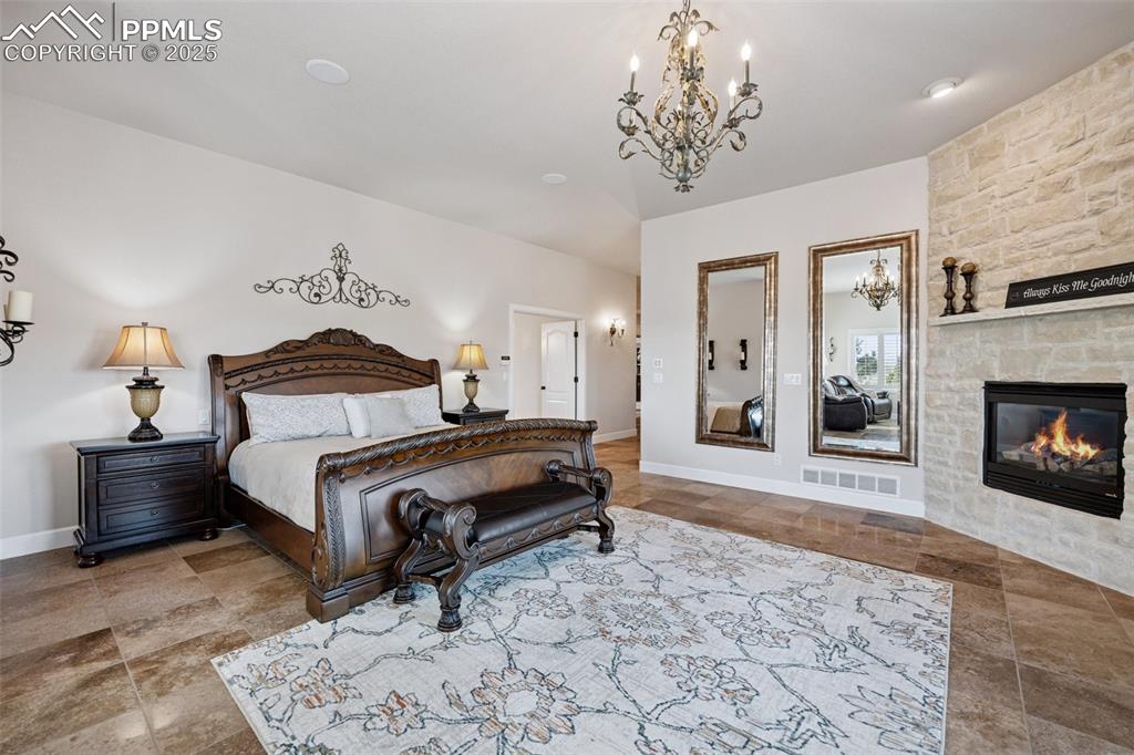 Image 22 of 48: Bedroom with baseboards, a stone fireplace, visible vents, and a chandelier