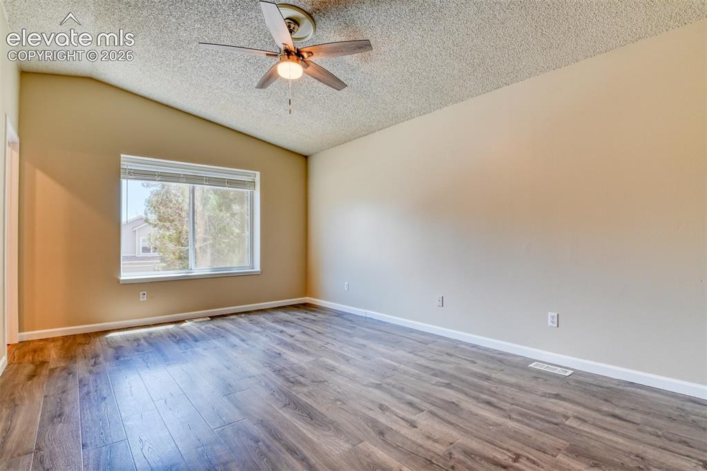 Image 18 of 50: Spacious room featuring vaulted ceilings, wood-finish flooring, a ceiling f