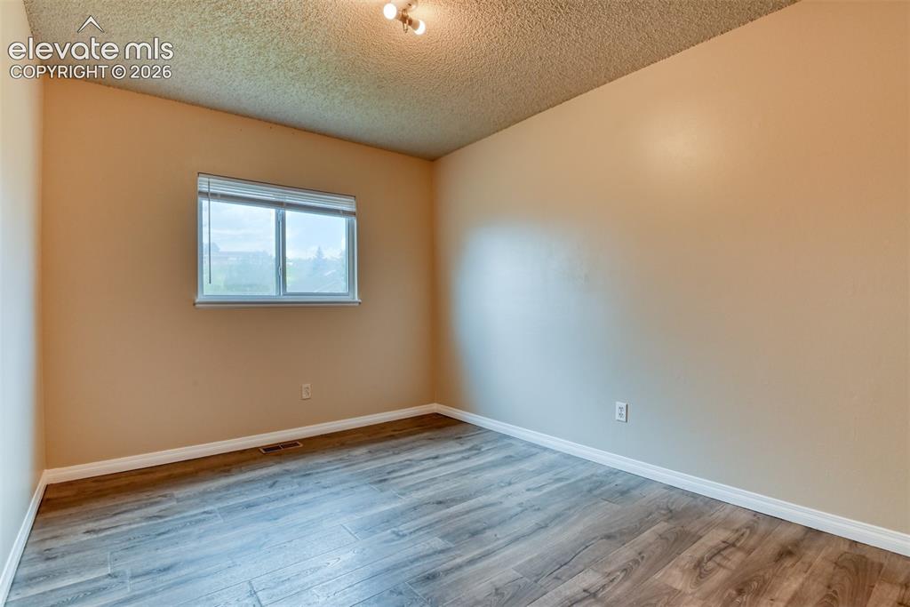 Image 25 of 50: Spacious room featuring wood-finish flooring, light tan walls, white trim,