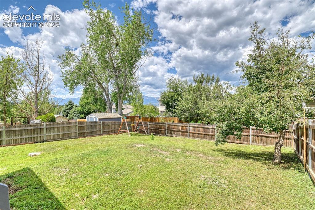 Image 42 of 50: Expansive fenced yard featuring a manicured lawn, mature trees, and a stora