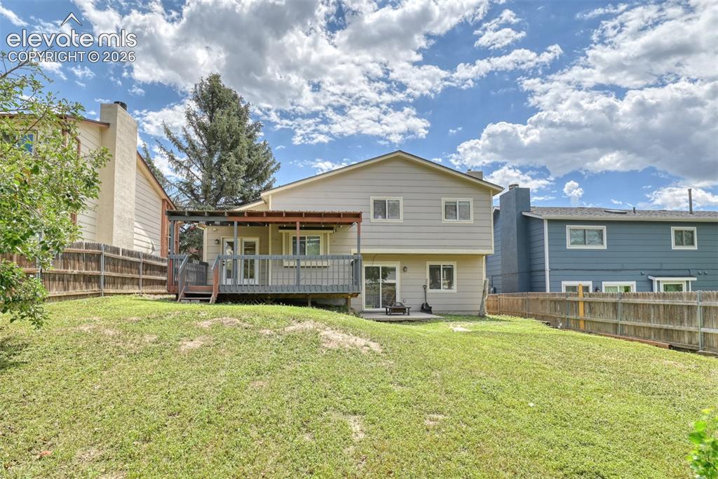 Image 43 of 50: Expansive sloped lawn with a two-story exterior featuring a covered wood de