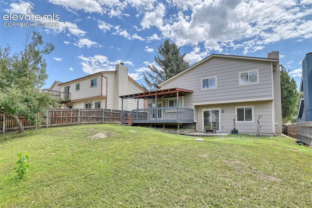 Image 44 of 50: Expansive sloped lawn with a perimeter wood fence, covered deck, and lower
