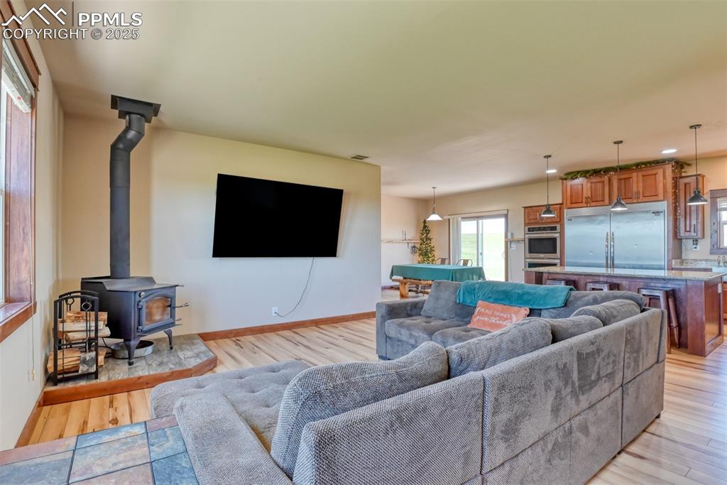 Image 11 of 47: Living area with a wood stove, light wood finished floors, and pool table