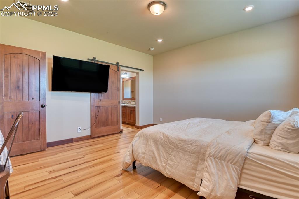 Image 14 of 47: Bedroom with LVT wood style floors, a barn door, recessed lighting, and ens