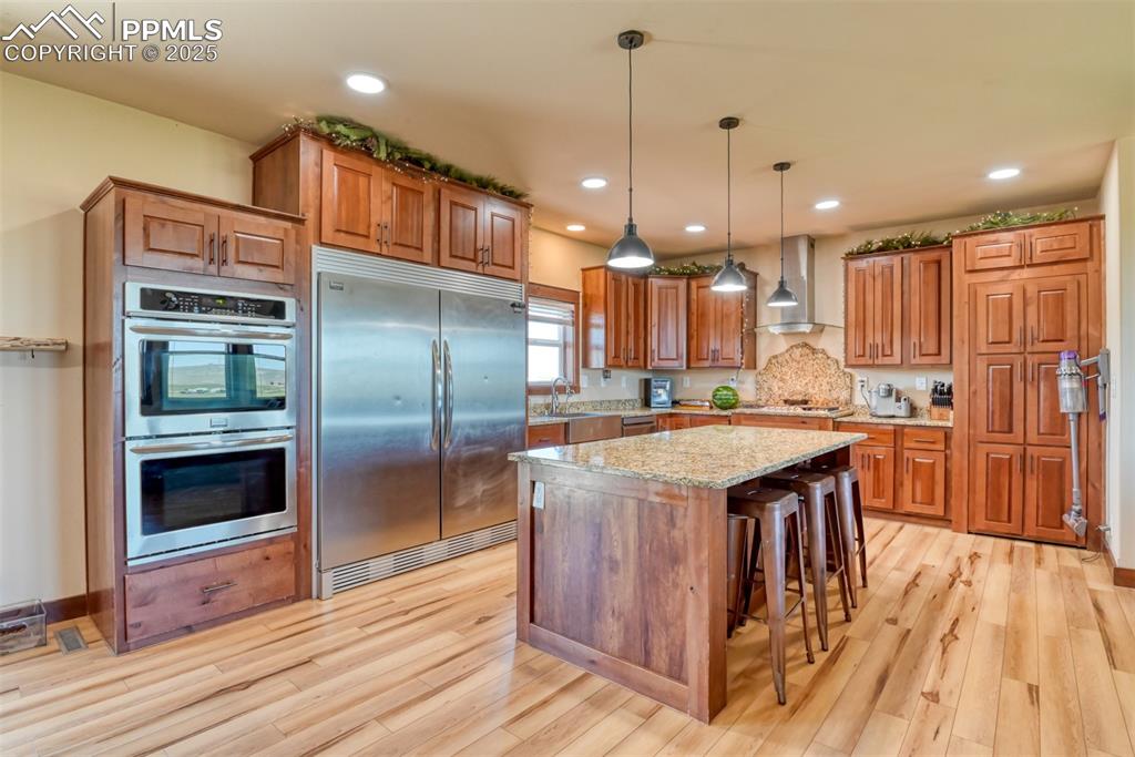 Image 2 of 47: Kitchen with stainless steel appliances, wall chimney range hood, brown cab