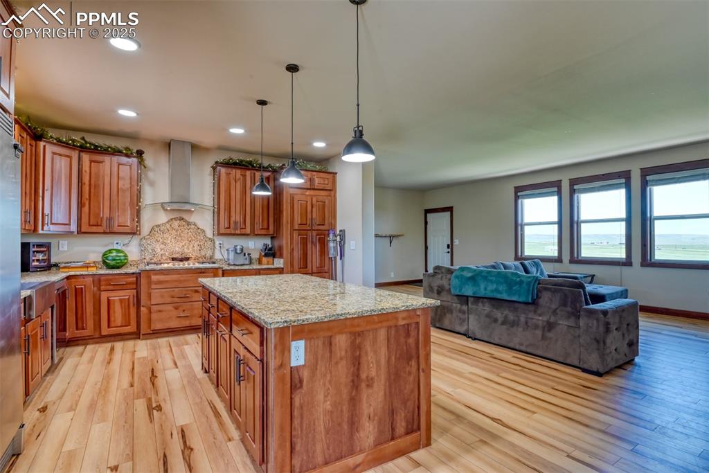 Image 3 of 47: Kitchen featuring wall chimney range hood, brown cabinets, light wood-style