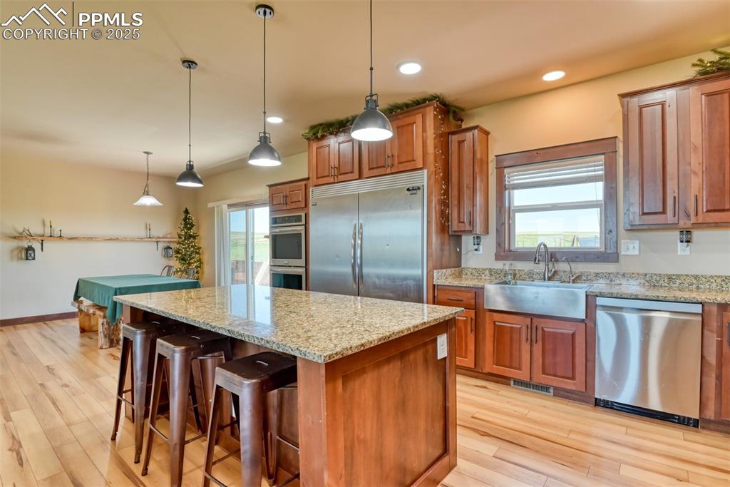 Image 4 of 47: Kitchen featuring stainless steel appliances, brown cabinets, light stone c