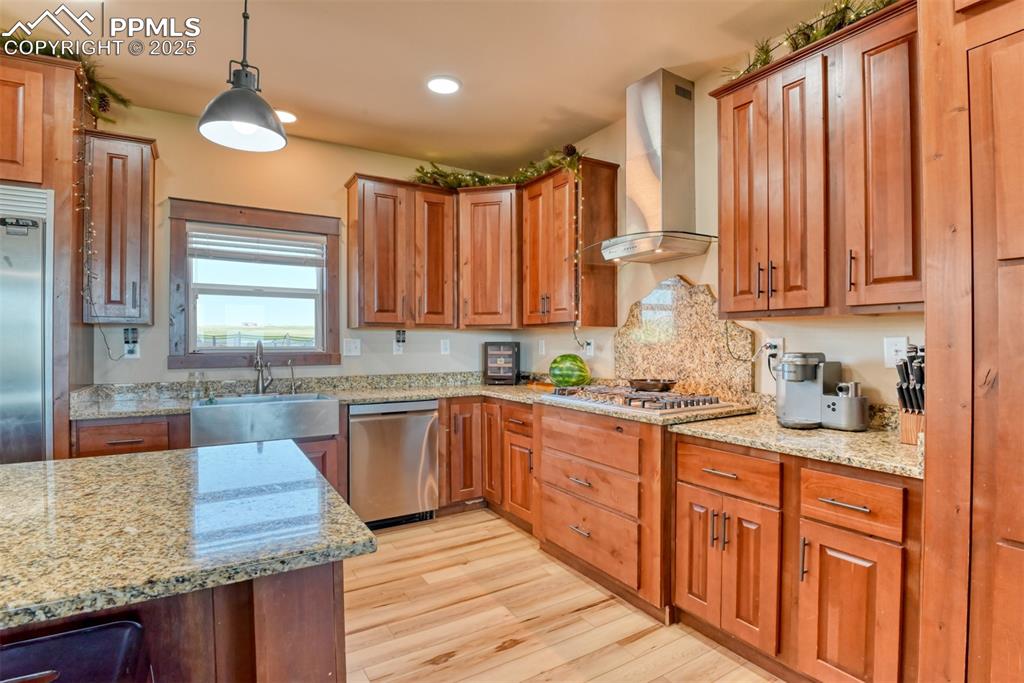 Image 6 of 47: Kitchen with wall chimney range hood, light wood-style flooring, appliances