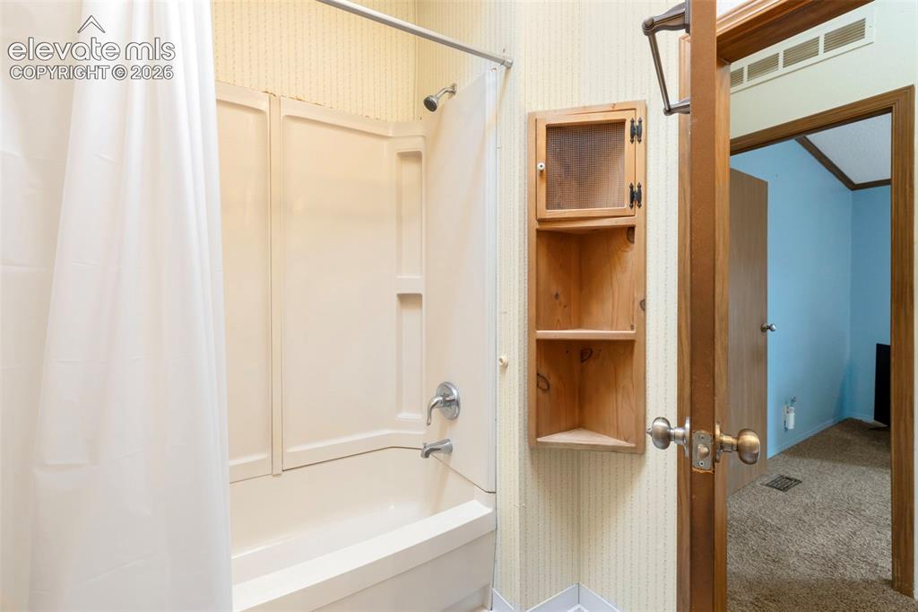 Image 23 of 38: Bathtub with integrated shower surround and chrome fixtures
