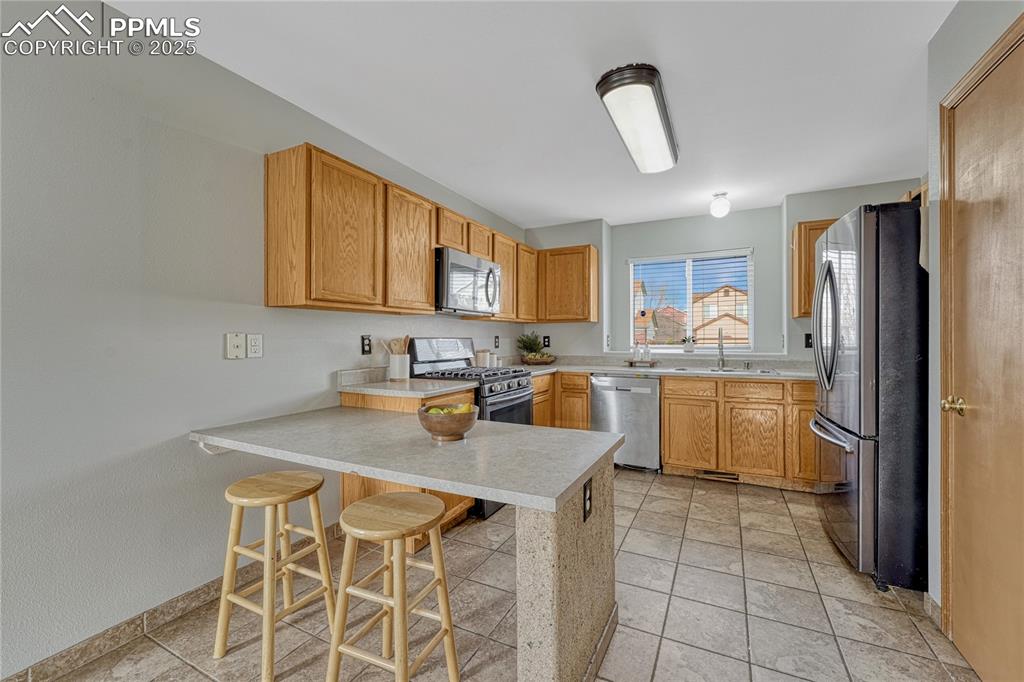 Image 20 of 47: Kitchen with counter bar, tile flooring, and window over kitchen sink