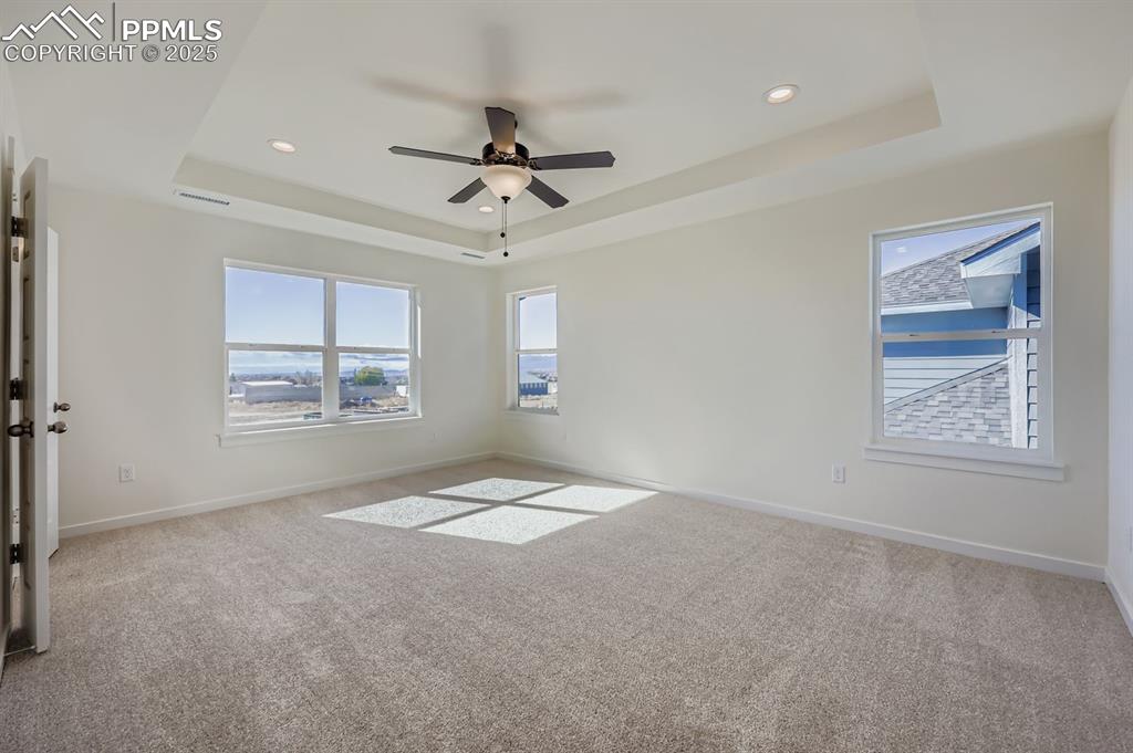 Image 12 of 28: Unfurnished room featuring a tray ceiling, light carpet, a ceiling fan, and