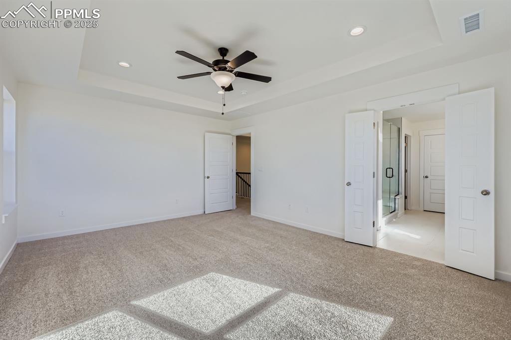 Image 13 of 28: Unfurnished bedroom featuring a tray ceiling, carpet floors, a ceiling fan,