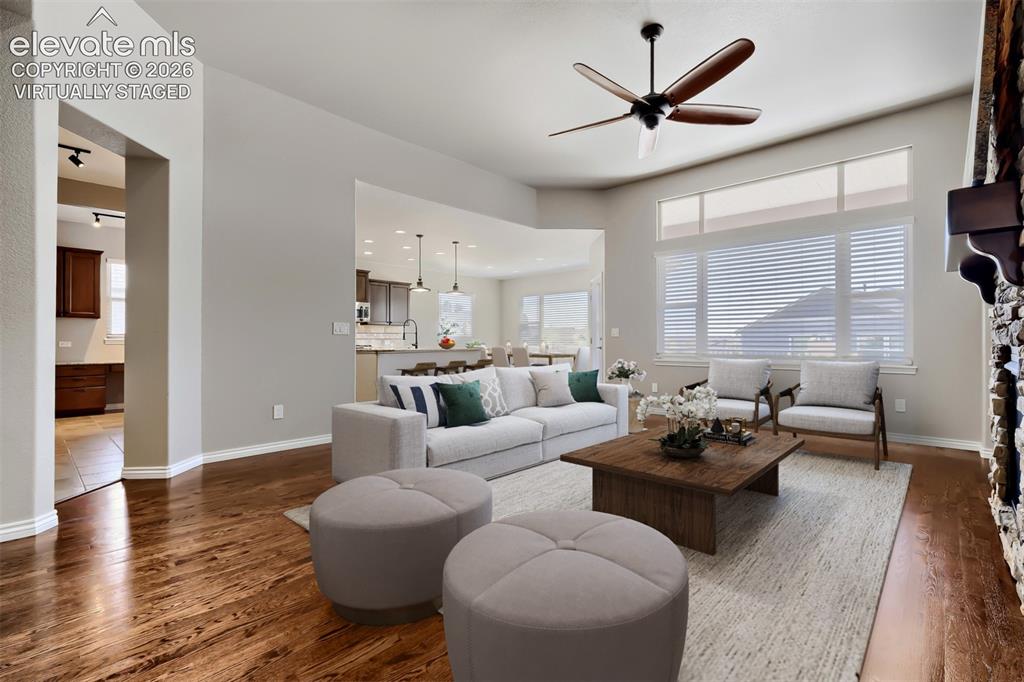 Image 4 of 50: Virtually staged living room with picture windows, stone fireplace, open c