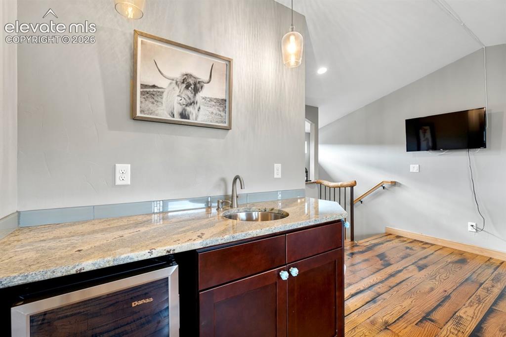 Image 19 of 50: Wet bar with granite countertop, stainless steel sink, and integrated bever