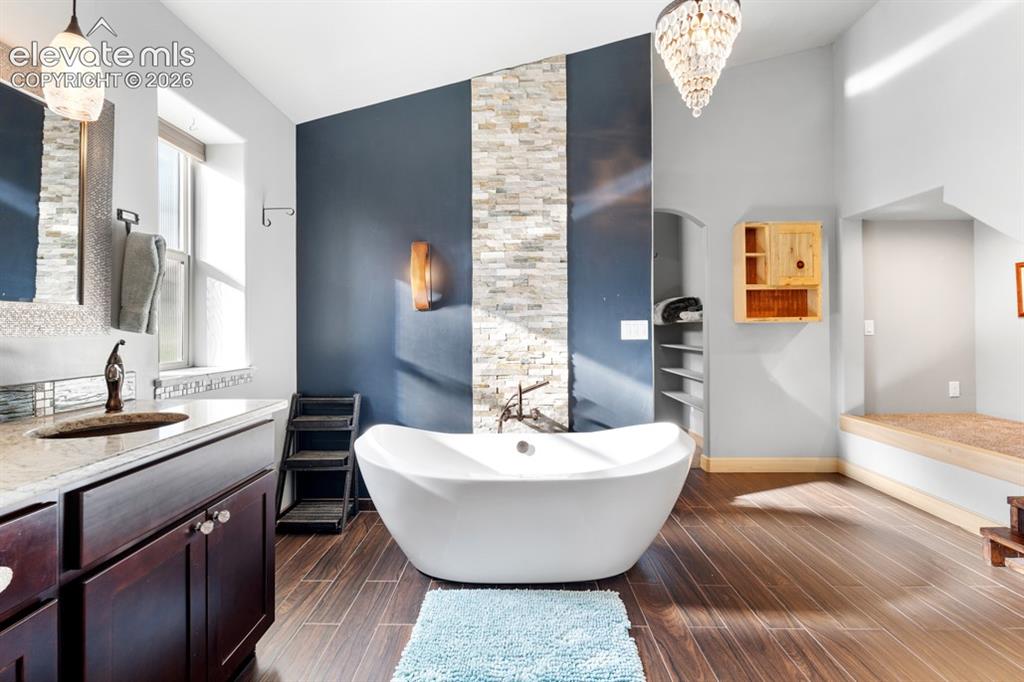 Image 32 of 50: Freestanding soaking tub with dark wood-finish flooring, a stacked stone ac