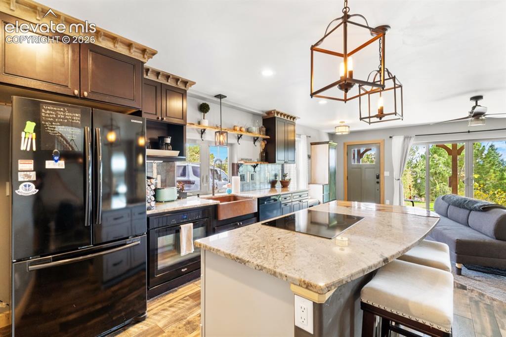 Image 44 of 50: Kitchen featuring wood-finish flooring, dark wood cabinetry, granite counte