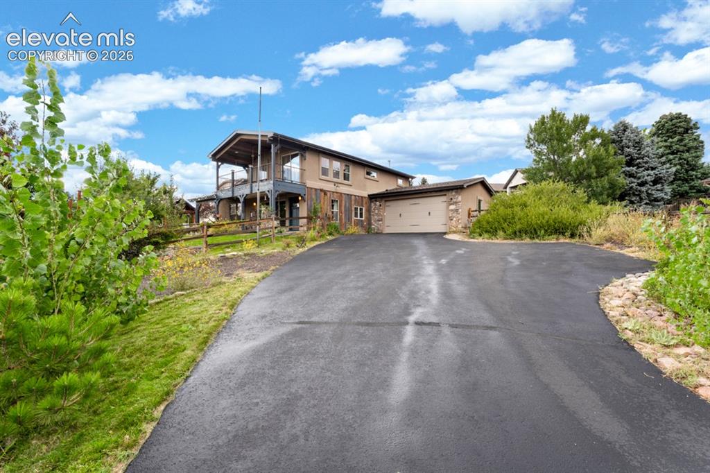 Image 8 of 50: Paved driveway leading to a two-story residence featuring a covered balcony