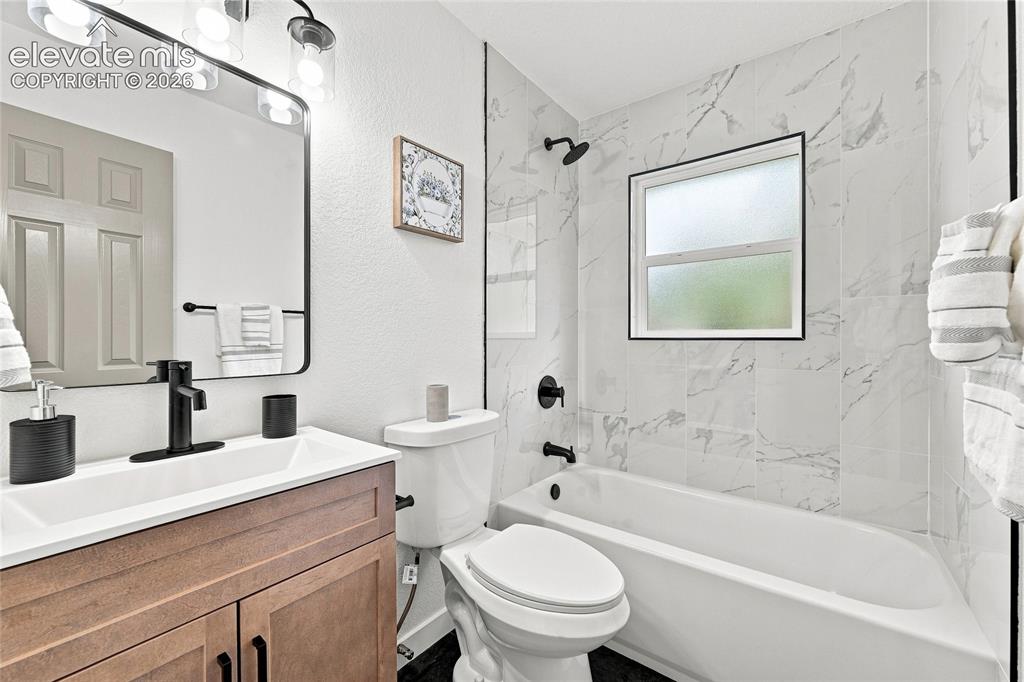 Image 15 of 30: Vanity with wood-finish cabinetry, integrated sink, and matte black faucet