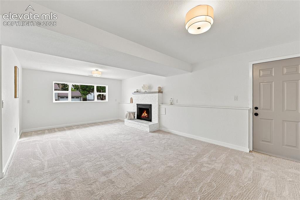 Image 18 of 30: Spacious room featuring light-toned carpeting, a white brick-surround firep