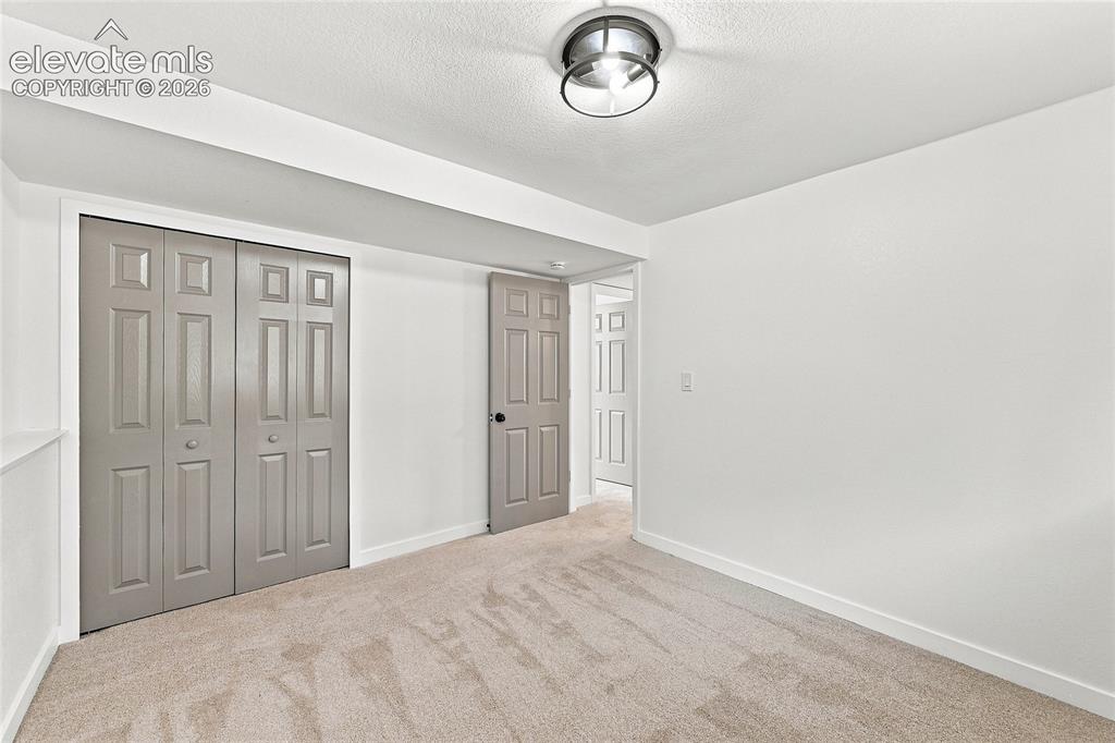 Image 22 of 30: Neutral wall color, wall-to-wall carpeting, bi-fold panel doors, and a flus