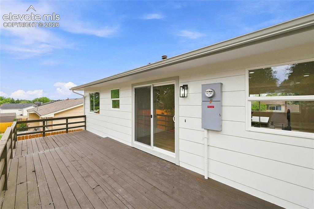 Image 23 of 30: Expansive wood deck with dark railings, white siding, and exterior lighting