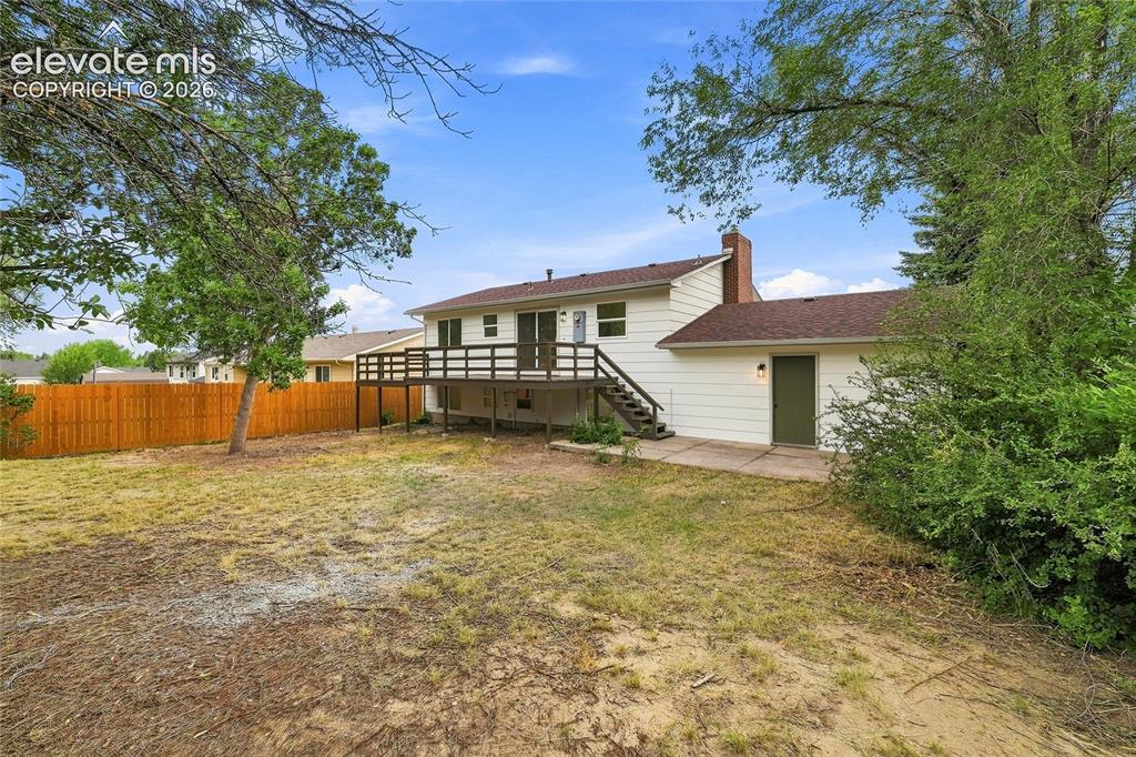 Image 25 of 30: Expansive backyard featuring a raised deck, a privacy fence, and mature tre