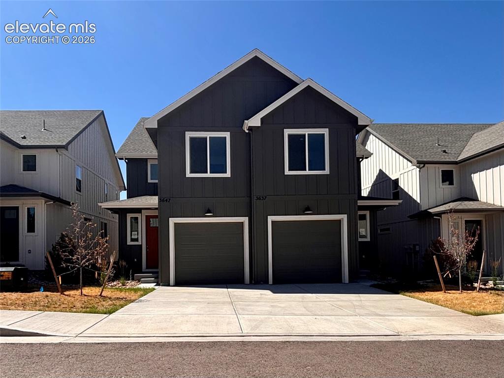 Caption: Modern townhome exterior featuring dark gray siding with white trim, two attached garages, and a red