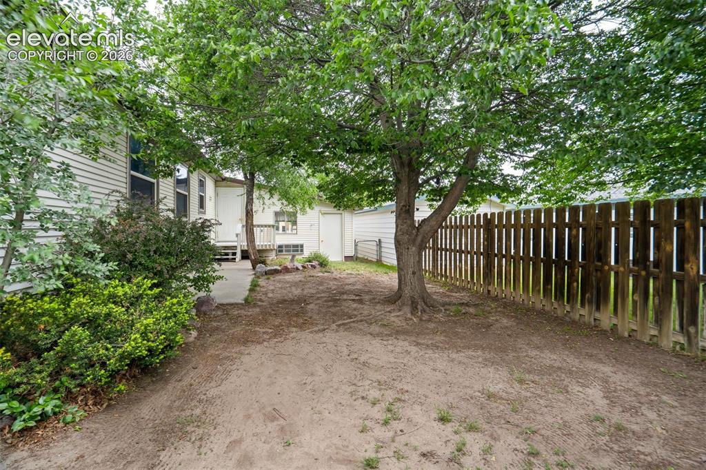 Image 42 of 50: Fenced backyard with mature trees providing shade and privacy.