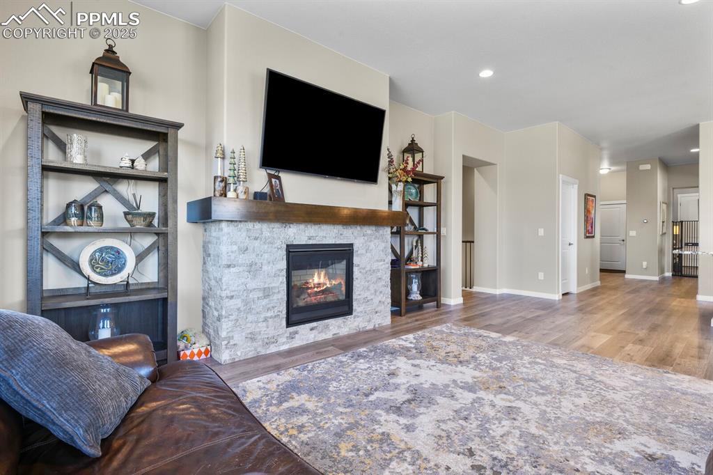 Image 11 of 50: Living room featuring a stone fireplace, wood finished floors, and recessed