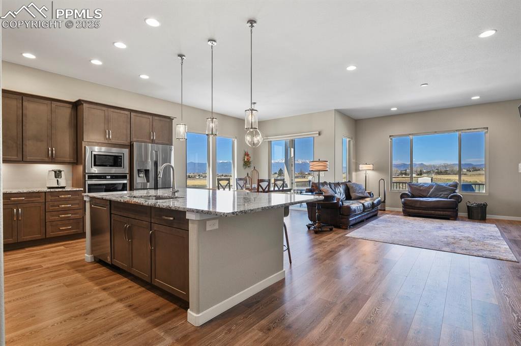 Image 13 of 50: Kitchen with a kitchen breakfast bar, dark wood-style floors, light stone c