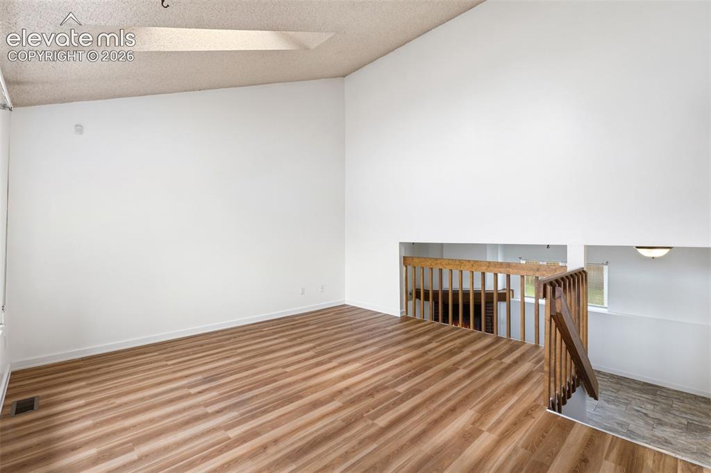 Image 10 of 43: Spacious room featuring vaulted ceilings, wood-finish flooring, white walls