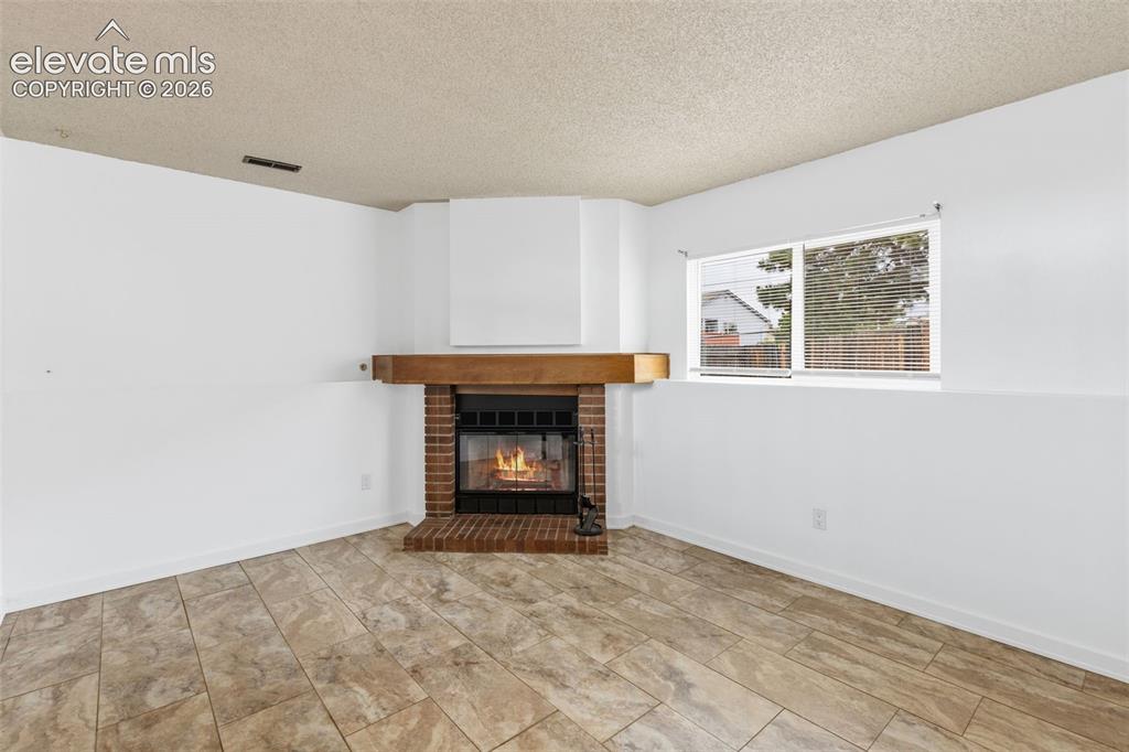Image 24 of 43: Corner fireplace featuring a brick surround and wood mantle