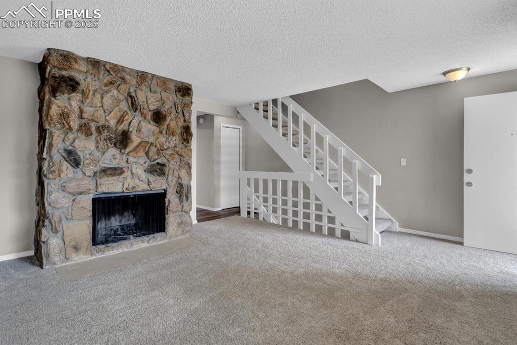 Image 4 of 28: Unfurnished living room with a textured ceiling, carpet floors, stairway, b