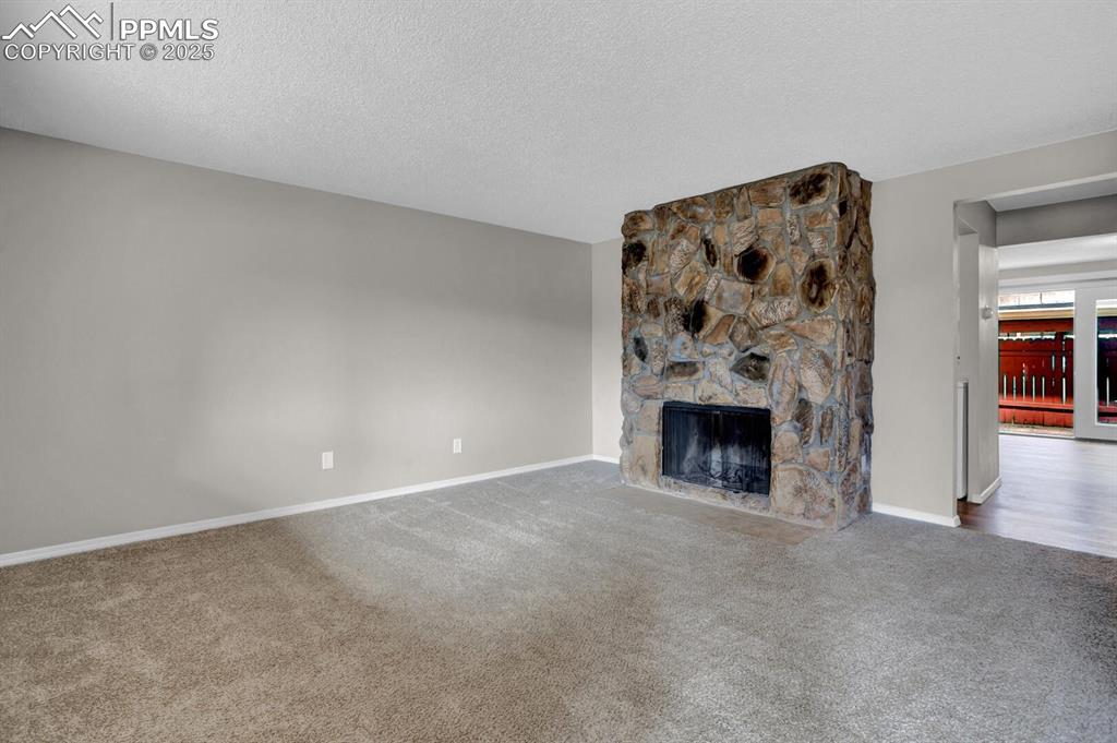 Image 5 of 28: Unfurnished living room featuring carpet flooring, baseboards, a stone fire