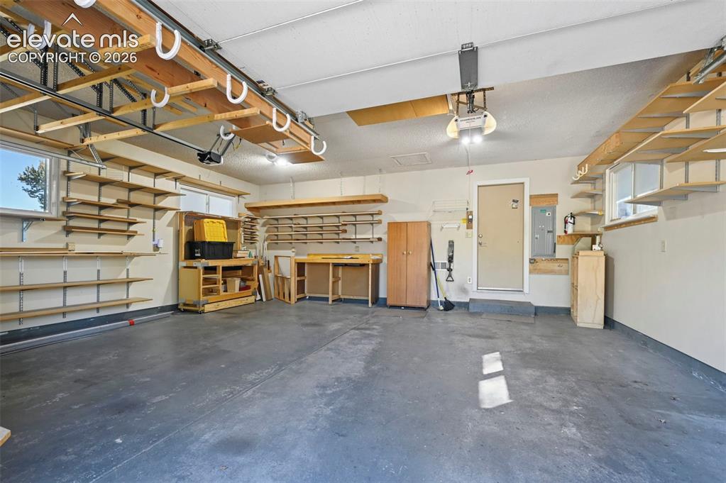Image 38 of 50: Spacious garage featuring extensive built-in shelving, concrete flooring, a