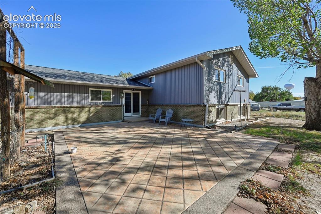 Image 42 of 50: Expansive rear patio area featuring a tiled surface and brick accents