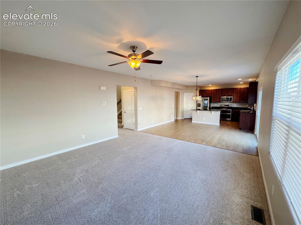 Image 12 of 42: Living area featuring neutral carpeting and a ceiling fan, kitchen with dar