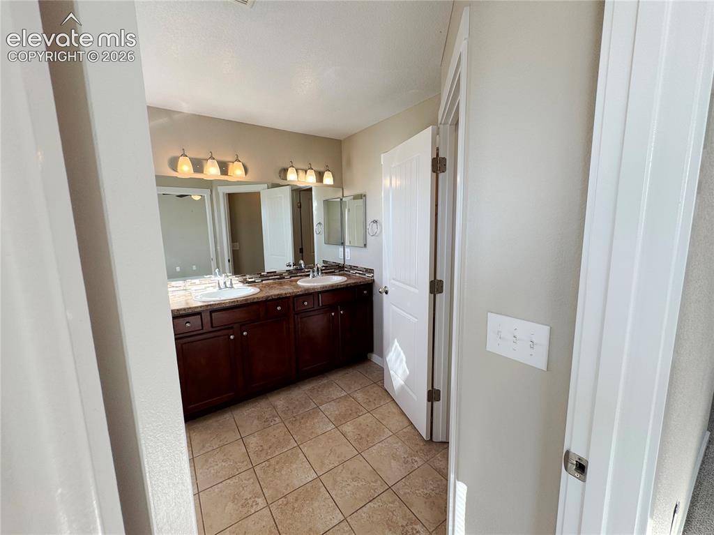 Image 32 of 42: Dual-sink vanity with dark wood cabinetry, stone-finish countertops, tiled