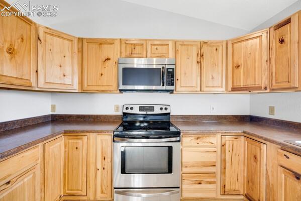 Image 11 of 26: Kitchen featuring stainless steel appliances, light brown cabinets, vaulted
