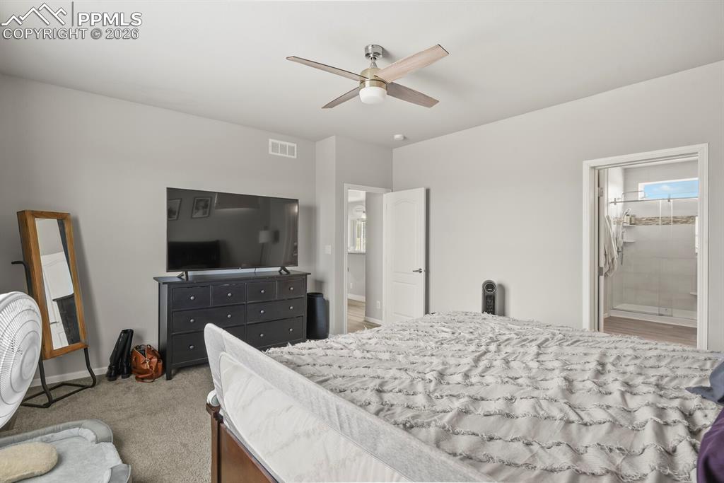 Image 19 of 48: Carpeted bedroom featuring a ceiling fan, light gray walls, and a doorway l