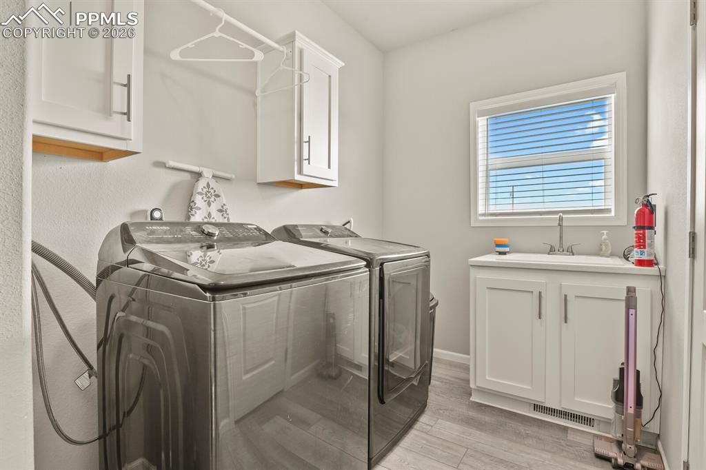 Image 27 of 48: Dedicated laundry area featuring a utility sink, white cabinetry with conte